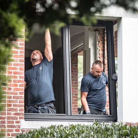Two men installing black aluminium window in private renovation.